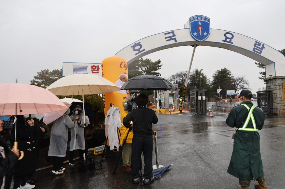 A South Korean soldier (R) stands as reporters and BTS fans gather in front of the main gate of a military boot camp in Nonsan on December 11, 2023, where BTS members RM and V are scheduled to arrive to begin their military service. Photo by YONHAP / AFP