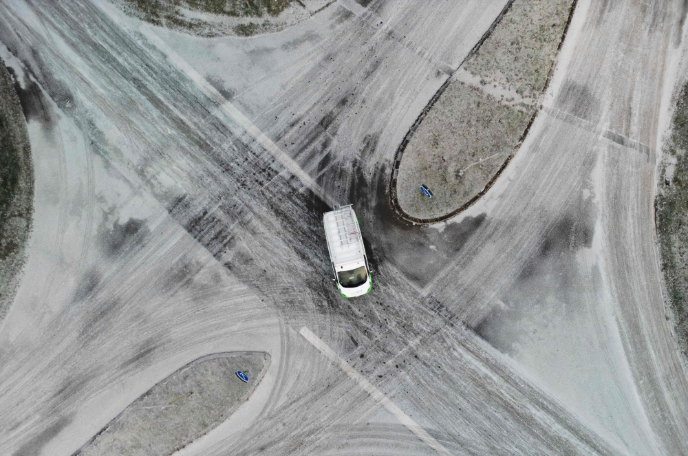 This aerial view shows a car passing a snow-covered road intersection close to Saint-Pierre-de-Plesguen, western France, on January 9, 2024. (Photo by Damien MEYER / AFP)