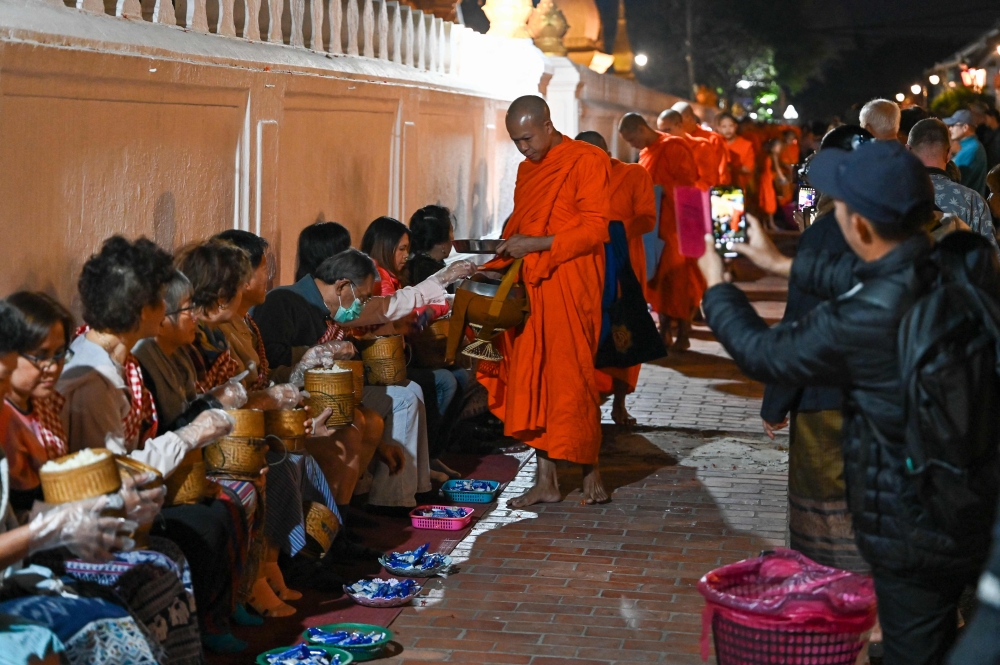 (Files) Buddhist monks line up at dawn to receive food and alms from devotees in front of a pagoda in Luang Prabang on January 28, 2024. (Photo by Tang Chhin Sothy / AFP)