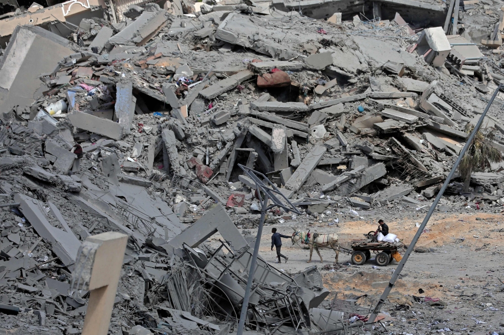 Displaced Palestinians transport their belongings on a horsecart through a street amid the rubble of houses destroyed by Israeli bombardment in Hamad area, west of Khan Yunis in the southern Gaza Strip on March 14, 2024. (Photo by AFP)
