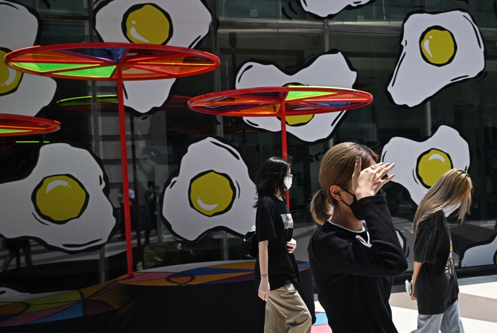 (Files) Pedestrians shield themselves from the sun to combat the heat outside Siam Paragon shopping mall in Bangkok on April 1, 2024. (Photo by Lillian Suwanrumpha / AFP)