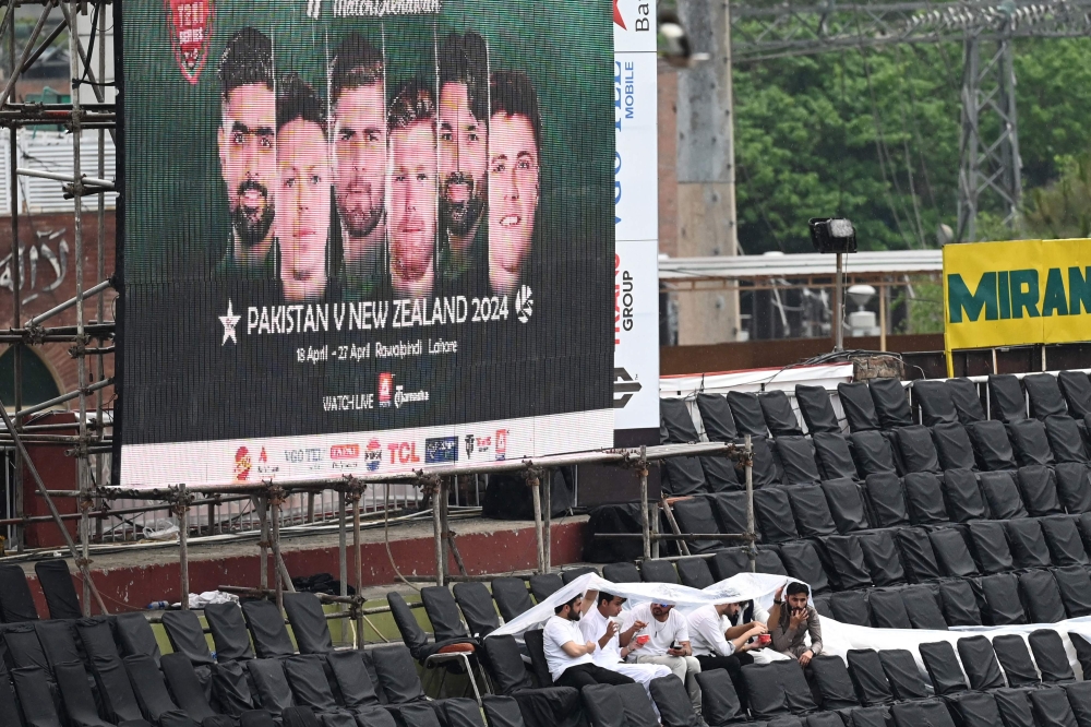 Spectators sit under a plastic sheet in stands during rainfall before the start of the first Twenty20 international cricket match between Pakistan and New Zealand at the Rawalpindi Cricket Stadium in Rawalpindi on April 18, 2024. (Photo by Aamir Qureshi / AFP)