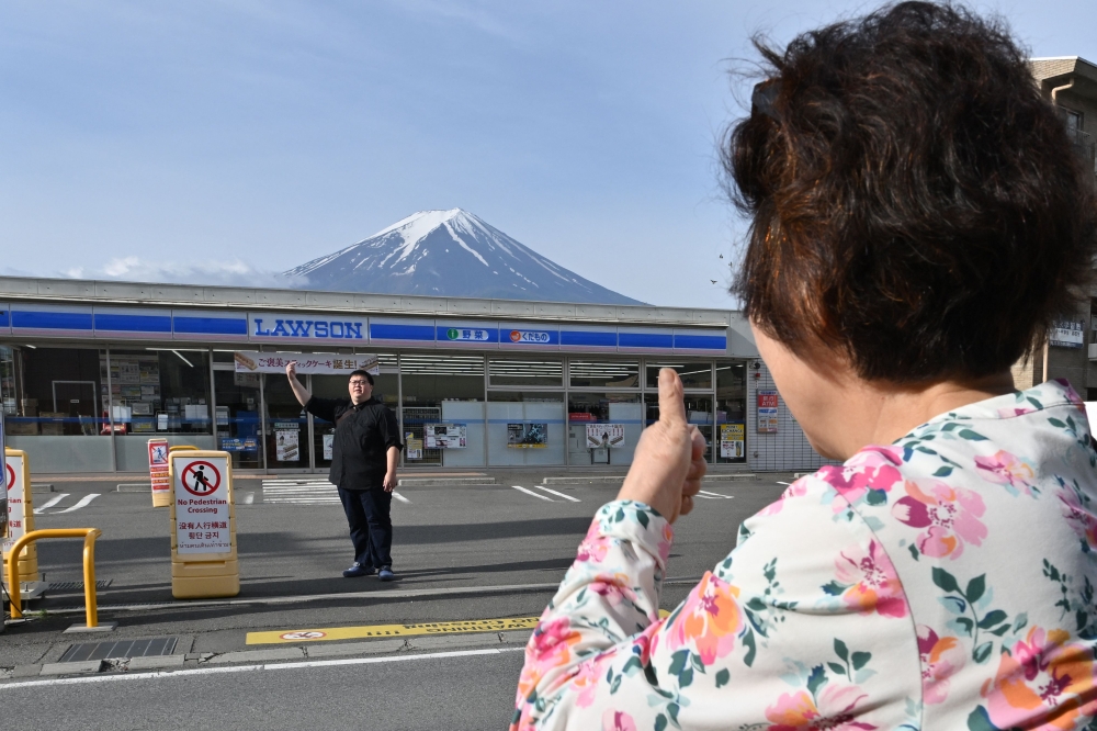 A person takes pictures of Mount Fuji from across the street of a convenience store, hours before the installation of a barrier to block the sight of Japan's Mount Fuji to deter badly behaved tourists, in the town of Fujikawaguchiko, Yamanashi prefecture on May 21, 2024. Photo by Kazuhiro NOGI / AFP