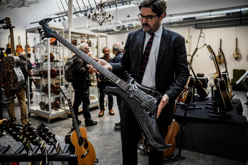 Auctioneer Etienne De Baecque holds the Warwick 4-string Buzzard bass guitar designed by John Entwistle, bassist of famous rock band The Who in a room of De Baecke auction house, in Lyon, on May 22, 2024 as people examine music instruments on the eve of the auction. (Photo by Jeff Pachoud / AFP) /