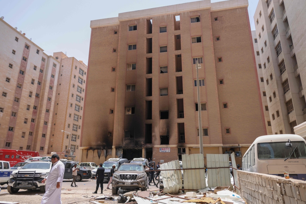 People walk past a building which was ingulfed by fire, in Kuwait City, on June 12, 2024. Photo by Yasser Al-Zayyat / AFP.