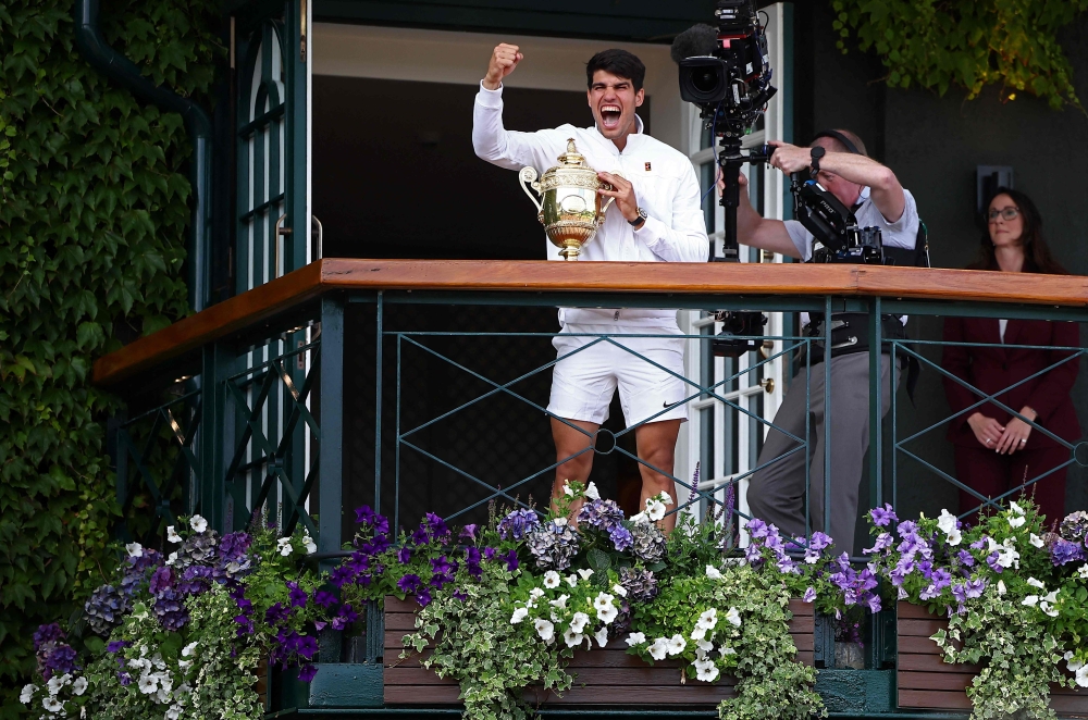 Spain's Carlos Alcaraz celebrates with the winner's trophy as he shows it to the crowd from the Centre Court balcony after winning against Serbia's Novak Djokovic during their men's singles final tennis match on the fourteenth day of the 2024 Wimbledon Championships at The All England Lawn Tennis and Croquet Club in Wimbledon, southwest London, on July 14, 2024. (Photo by HENRY NICHOLLS / AFP)
