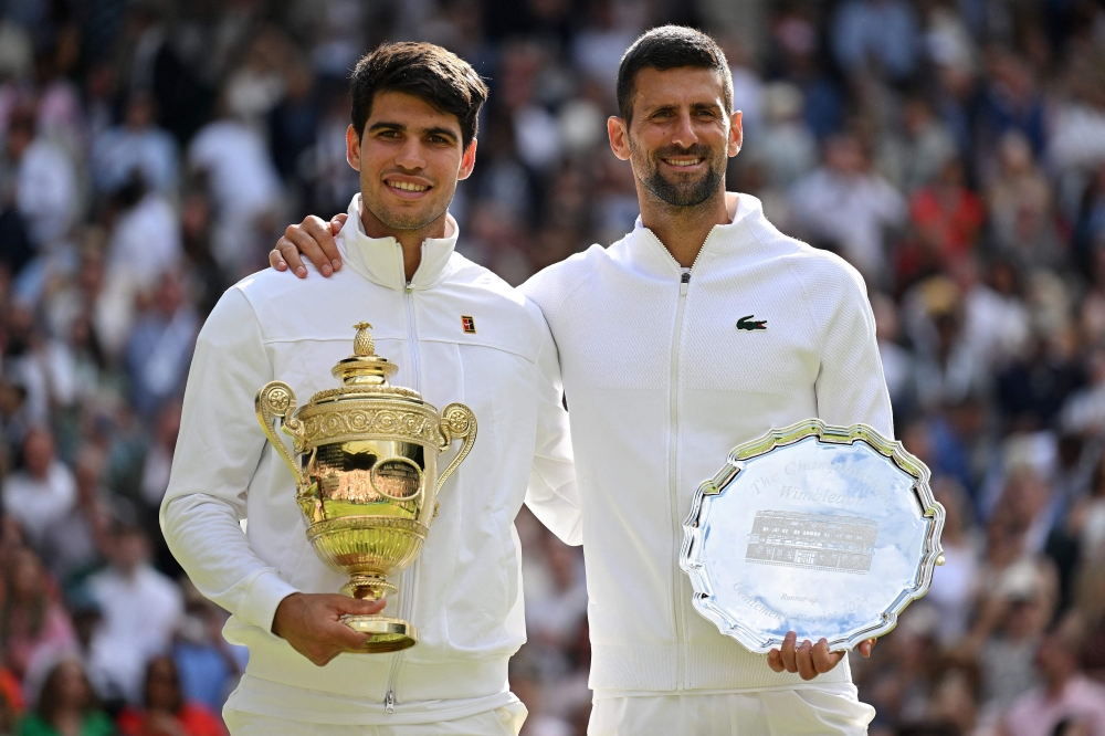 Spain's Carlos Alcaraz holding the winner's trophy (left) and second-placed Serbia's Novak Djokovic pose for pictures during the price ceremony at the end of their men's singles final tennis match on the fourteenth day of the 2024 Wimbledon Championships at The All England Lawn Tennis and Croquet Club in Wimbledon, southwest London, on July 14, 2024. (Photo by Andrej Isakovic / AFP) 