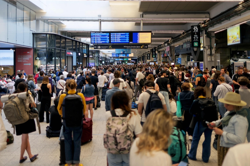 Passengers gather around the departure boards at the Gare Montparnasse train station in Paris on July 26, 2024 as France's high-speed rail network was hit by malicious acts disrupting the transport system hours before the opening ceremony of the Paris 2024 Olympic Games. Photo by Thibaud MORITZ / AFP