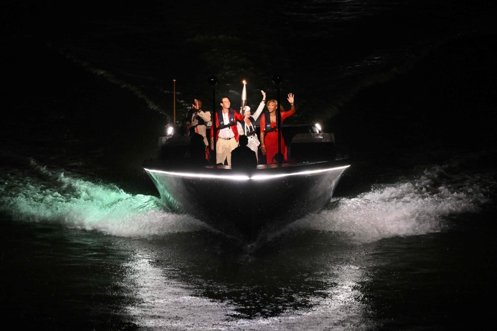 Spanish tennis player Rafael Nadal (2L) holds the Olympic torch next to US' athlete Carl Lewis (L), Romanian gymnast Nadia Comaneci (2R) and US tennis player Serena Williams (R) on the river Seine during the opening ceremony of the Paris 2024 Olympic Games in Paris on July 26, 2024. (Photo by SEBASTIEN BOZON / AFP)
