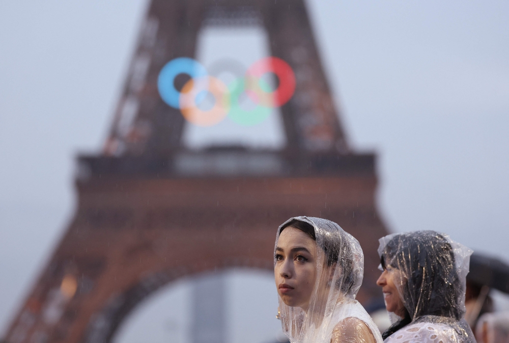 Spectators wear ponchos to shelter from the rain beside the Eiffel Tower during the opening ceremony of the Olympic Games Paris 2024 on July 26, 2024 in Paris, France. Photo by Cameron Spencer / POOL / AFP