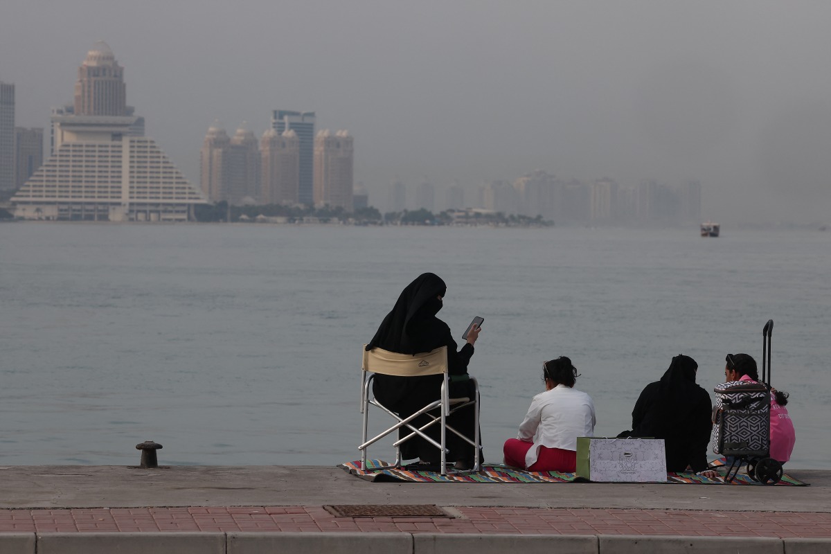 A family sits on the pavement by the Gulf waters on Doha's beachfront with the Qatari capital's landmark hotels and highrises in the background on August 6, 2024. (Photo by KARIM JAAFAR / AFP)