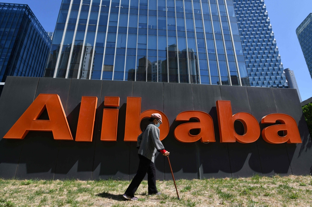 A woman walks past an Alibaba sign outside the company's office in Beijing on April 13, 2021. Photo by GREG BAKER / AFP