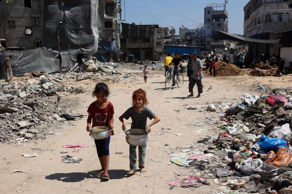 Palestinian children carry pots of soup near a food distribution point in the Jabalia refugee camp in northern Gaza Strip on August 21, 2024. (Photo by Omar Al-Qattaa / AFP)