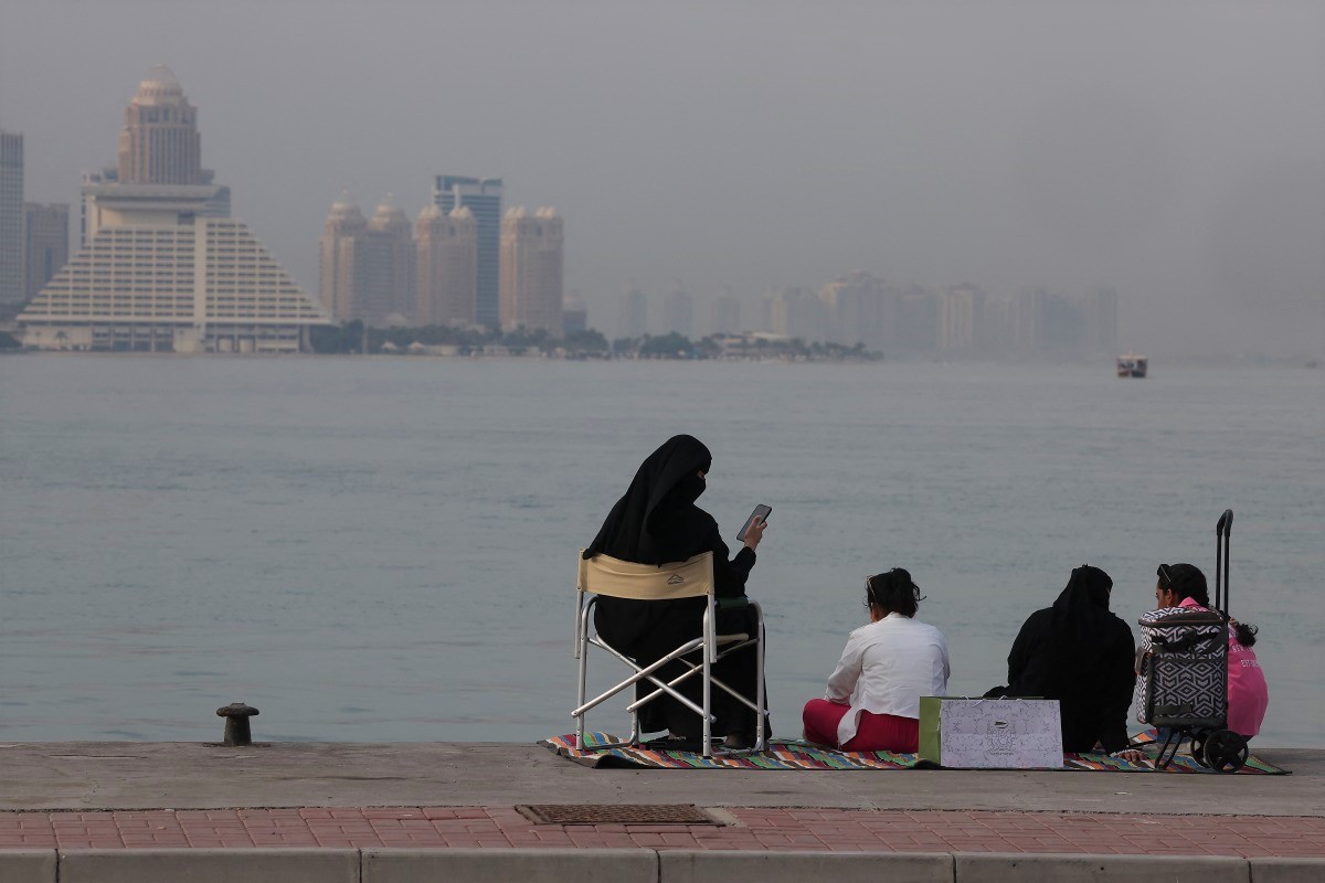 A family sits on the pavement along Doha Corniche on August 6, 2024. (Photo by Karim Jaafar / AFP)

