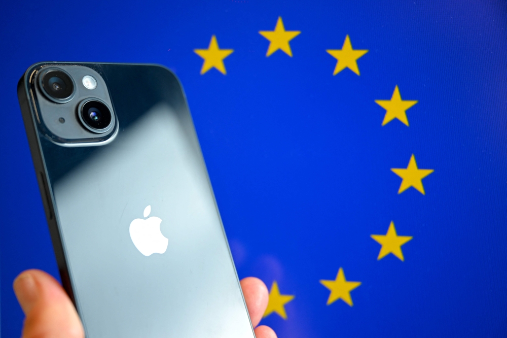 (Files) This photograph shows a hand-held smartphone with the Apple company logo and the European Union logo in the background, in Brussels on September 9, 2024. (Photo by Nicolas TUCAT / AFP)