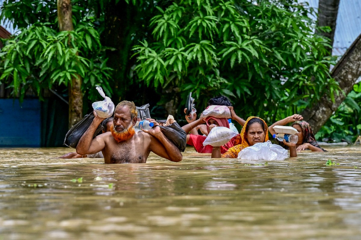 People carrying relief materials wade through flood waters in Feni, in south-eastern Bangladesh, on August 24, 2024. (Photo by Munir Uz Zaman / AFP.)