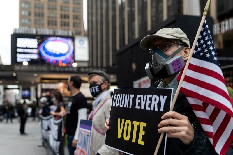 File photo for representational purposes only: A man wearing a protective mask due to COVID-19 pandemic holds a sign outside Madison Square Garden, which is used as a polling station, on the first day of early voting in Manhattan, New York, U.S. October 24, 2020. REUTERS/Jeenah Moon/File P