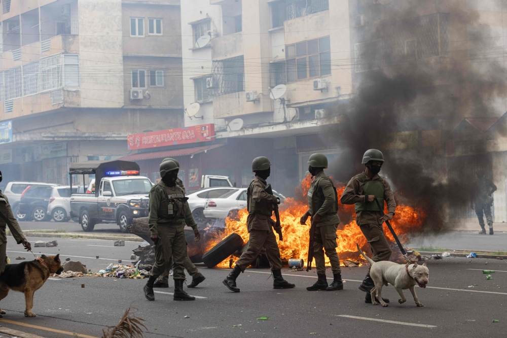 Anti-riot police officers with their dogs walk down Eduardo Mondlane Avenue past burning barricades made by protesters in Maputo November 7, 2024. (Photo by Alfredo Zuniga / AFP)