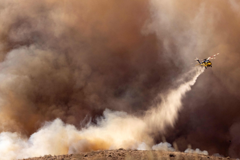 A fire helicopter makes a drop over the Mountain Fire as it scorches acres, the wildfire fueled by strong Santa Ana winds, in Moorpark, California, on November 7, 2024. (Photo by Etienne Laurent / AFP) / 