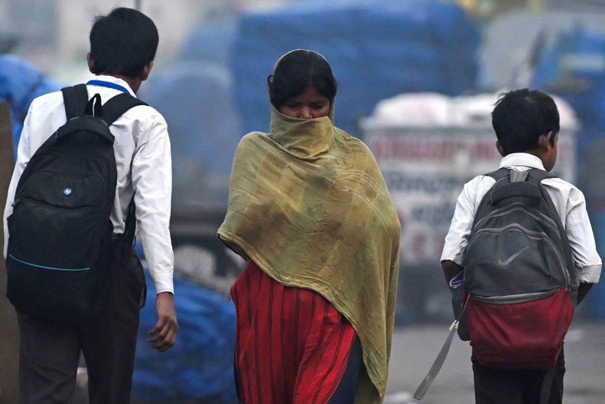 A woman covers her face as she walks past school boys on a cold smoggy morning in the old quarters of New Delhi on November 15, 2024. (Photo by Arun SANKAR / AFP)