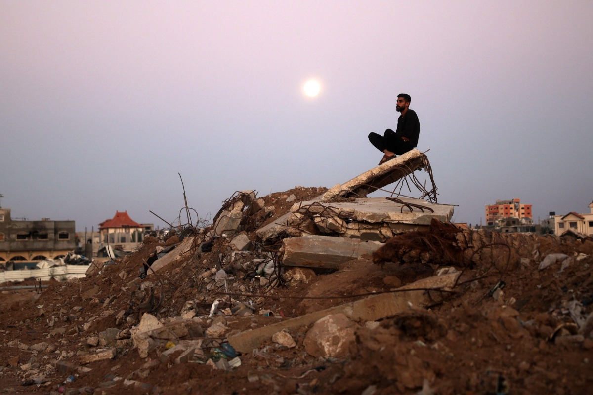 The full moon rises as a man sits atop a pile of rubble it the al-Bureij refugee camp in the central Gaza Strip on November 15, 2024, amid the ongoing war between Israel and the Hamas militant group. (Photo by Eyad BABA / AFP)