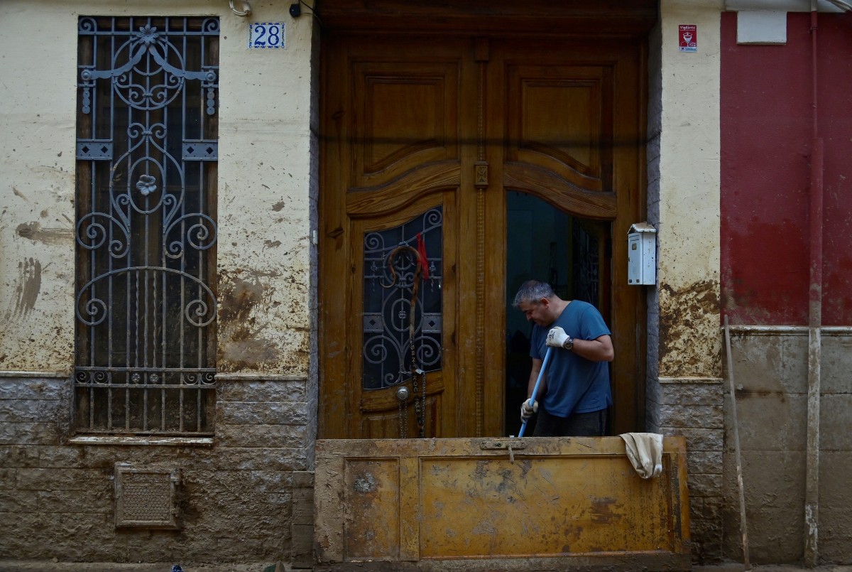 A man cleans his doorstep in Paiporta, south of Valencia, eastern Spain, on November 13, 2024 in the aftermath of deadly flooding. Photo by JOSE JORDAN / AFP