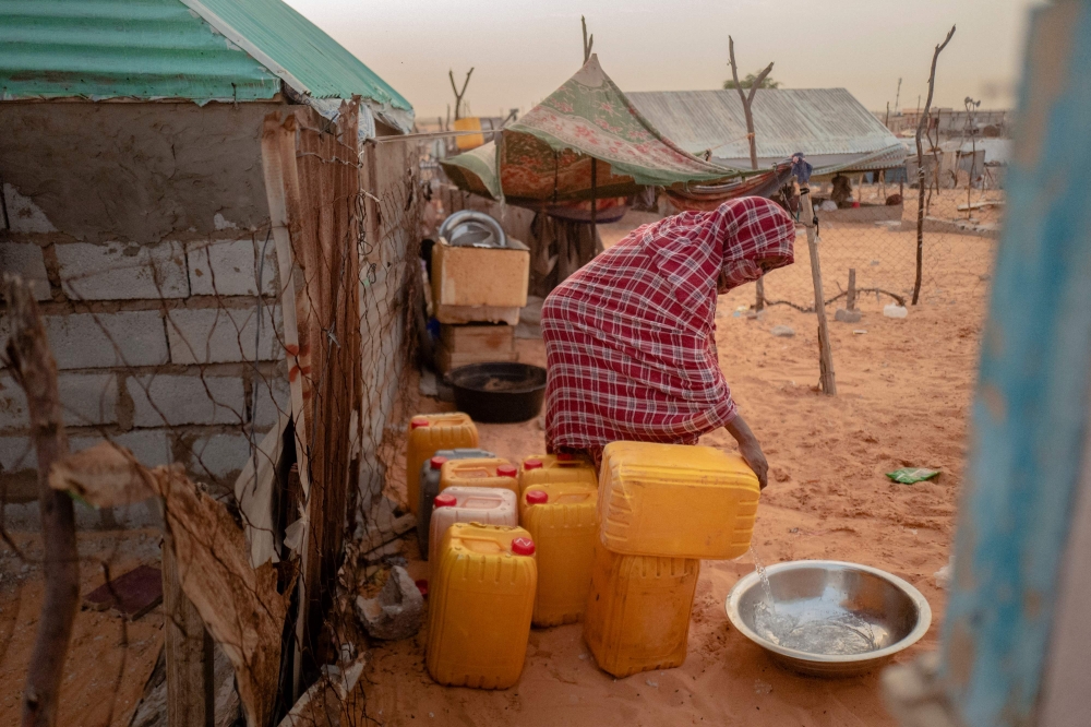 A woman pours water from a jerry can, in the Tarhil district, in Nouakchott, on September 30, 2024. (Photo by Michele Cattani / AFP)