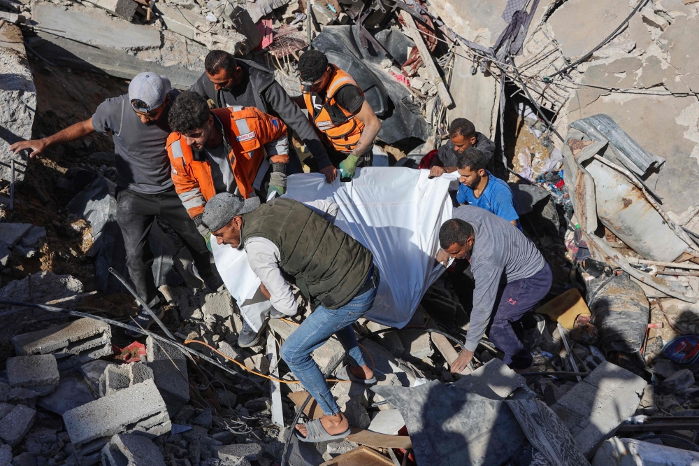 People and rescures carry the covered body of a preson pulled from the rubble of a house destroyed in an Israeli strike on al-Jalaa street in central Gaza City on November 18, 2024. (Photo by Omar Al-Qattaa / AFP)