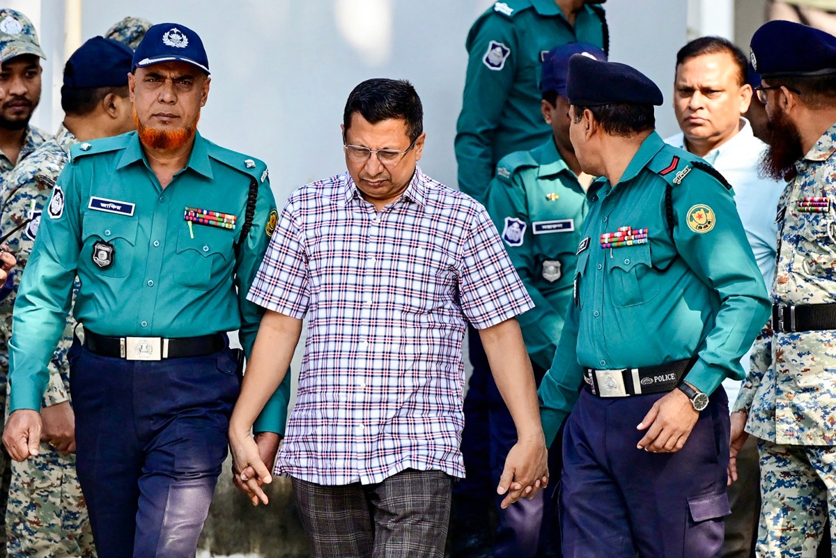 Police personnel escort detainees Chowdhury Abdullah Al-Mamun (C), a former police inspector general and Ziaul Ahsan (back 2R), a former military general and former director general of the National Telecommunication Monitoring Centre (NTMC), to Bangladesh's International Crimes Tribunal (ICT) court in Dhaka on November 20, 2024. Photo by Munir UZ ZAMAN / AFP.