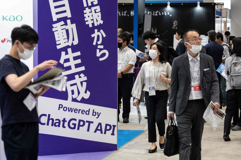 This file photo taken on May 10, 2023 shows visitors walking past a sign (L) promoting ChatGPT, a hugely popular language app that has sparked a rush in artificial intelligence technology, during the three-day 7th AI Expo, part of NexTech Week Tokyo 2023, Japan's largest trade show for artificial intelligence technology companies, at Tokyo Big Sight. Photo by Richard A. Brooks / AFP