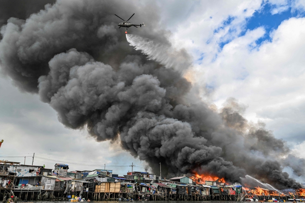 A Philippine Air Force helicopter drops water over houses on fire at Tondo in Manila on November 24, 2024. (Photo by Jam Sta Rosa / AFP)