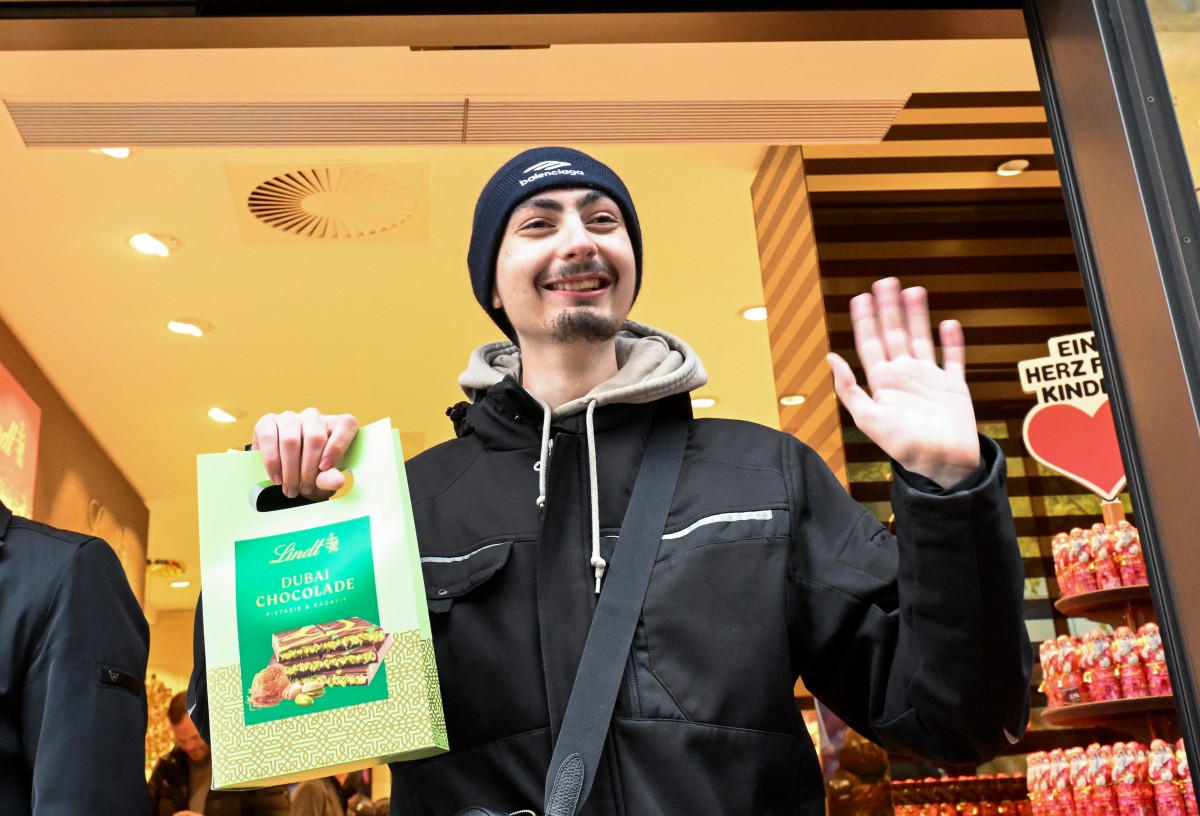 Leon Faehnle holds a Dubai Chocolate bar and smiles after he was the first customer after a ten hour wait who could buy one of 100 Dubai Chocolate bars in a branch of chocolate producer Lindt in Stuttgart, southern Germany, on November 15, 2024.Photo by THOMAS KIENZLE / AFP.