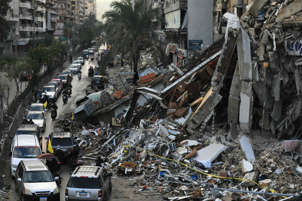 Motorists drive past a destroyed building in Beirut's southern suburbs on November 27, 2024, after a ceasefire took effect. (Photo by AFP)
 