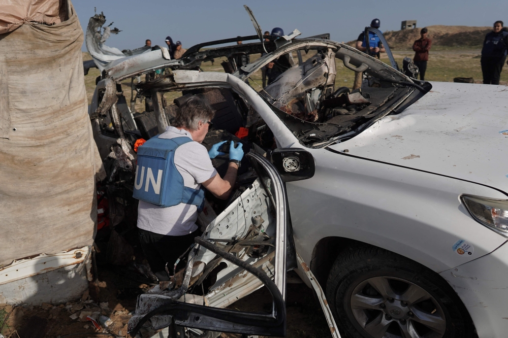 File photo used for representational purposes. United Nations staff members inspect the carcass of a car used by US-based aid group World Central Kitchen, that was hit by an Israeli strike the previous day in Deir al-Balah in the central Gaza Strip on April 2, 2024. Photo by AFP.