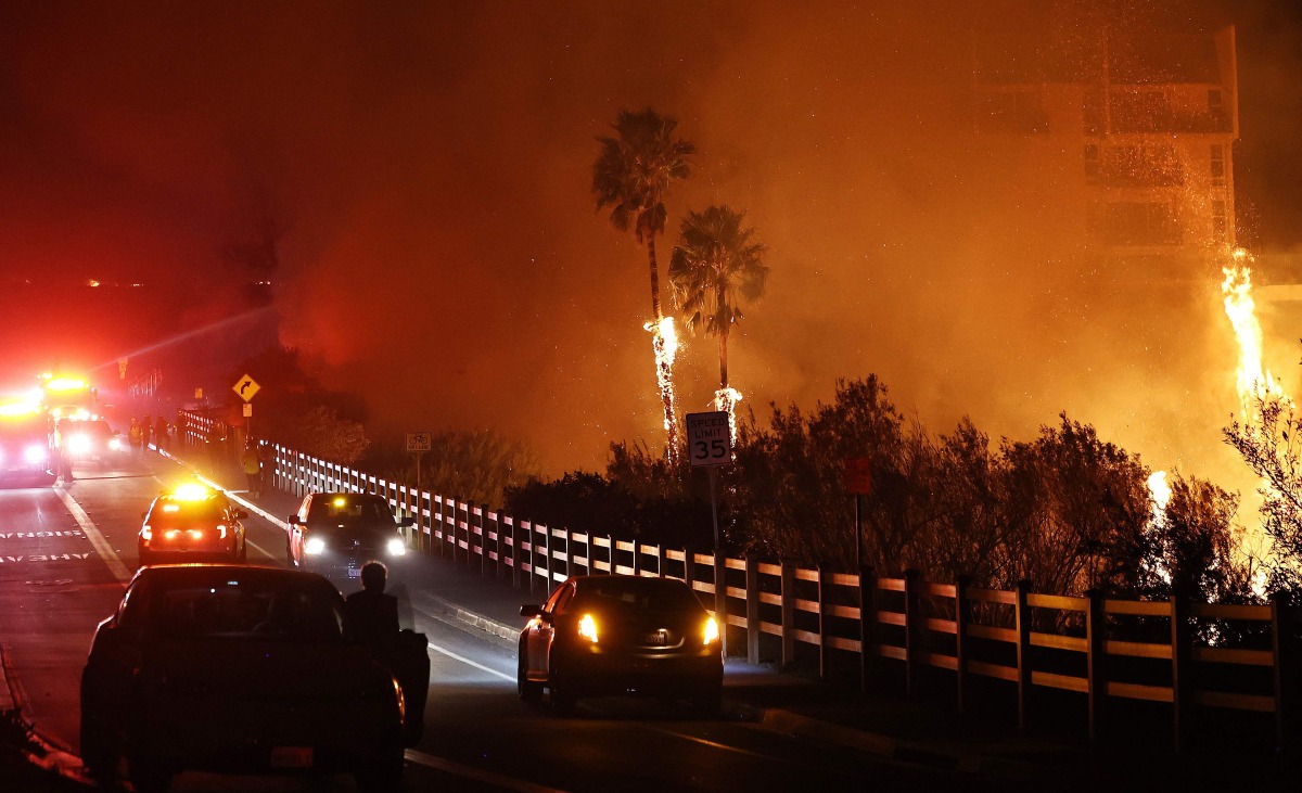 Firefighters work as the Franklin Fire burns near a building on December 10, 2024 in Malibu, California. Photo by MARIO TAMA / GETTY IMAGES NORTH AMERICA / Getty Images via AFP