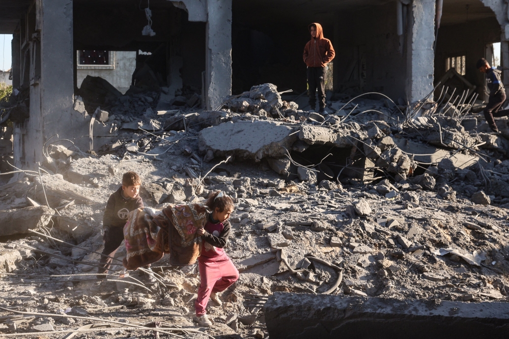 Palestinian children salvage a blanket amid the destruction in the aftermath of an Israeli strike in the al-Maghazi refugee camp in the central Gaza Strip on January 3, 2025. (Photo by Eyad Baba / AFP)
