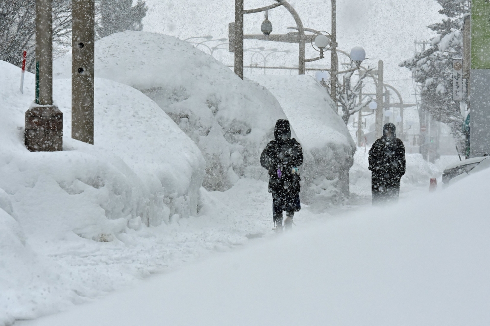 Pedestrians walk past high drifts of snow along a street in the northern Japanese city of Aomori on January 9, 2025. (Photo by JIJI Press / AFP) / Japan OUT