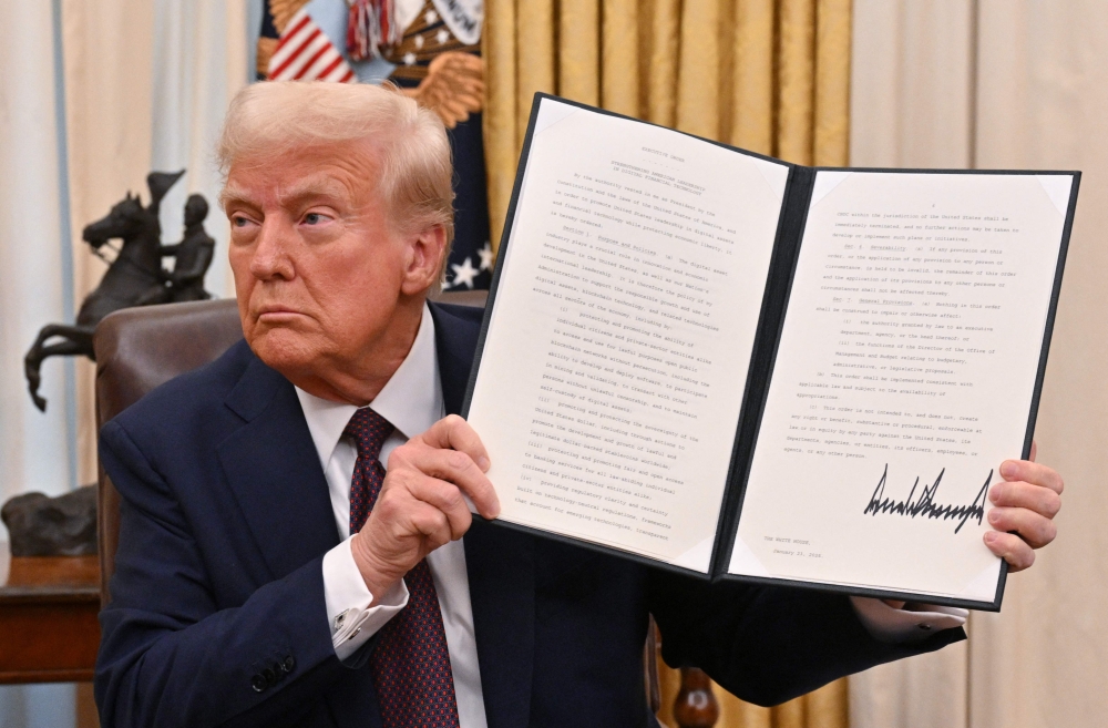 US President Donald Trump holds up an executive order he just signed to strenghten American leadership in digital financial technology, in the Oval Office of the White House in Washington, DC, on January 23, 2025. (Photo by Roberto Schmidt / AFP)