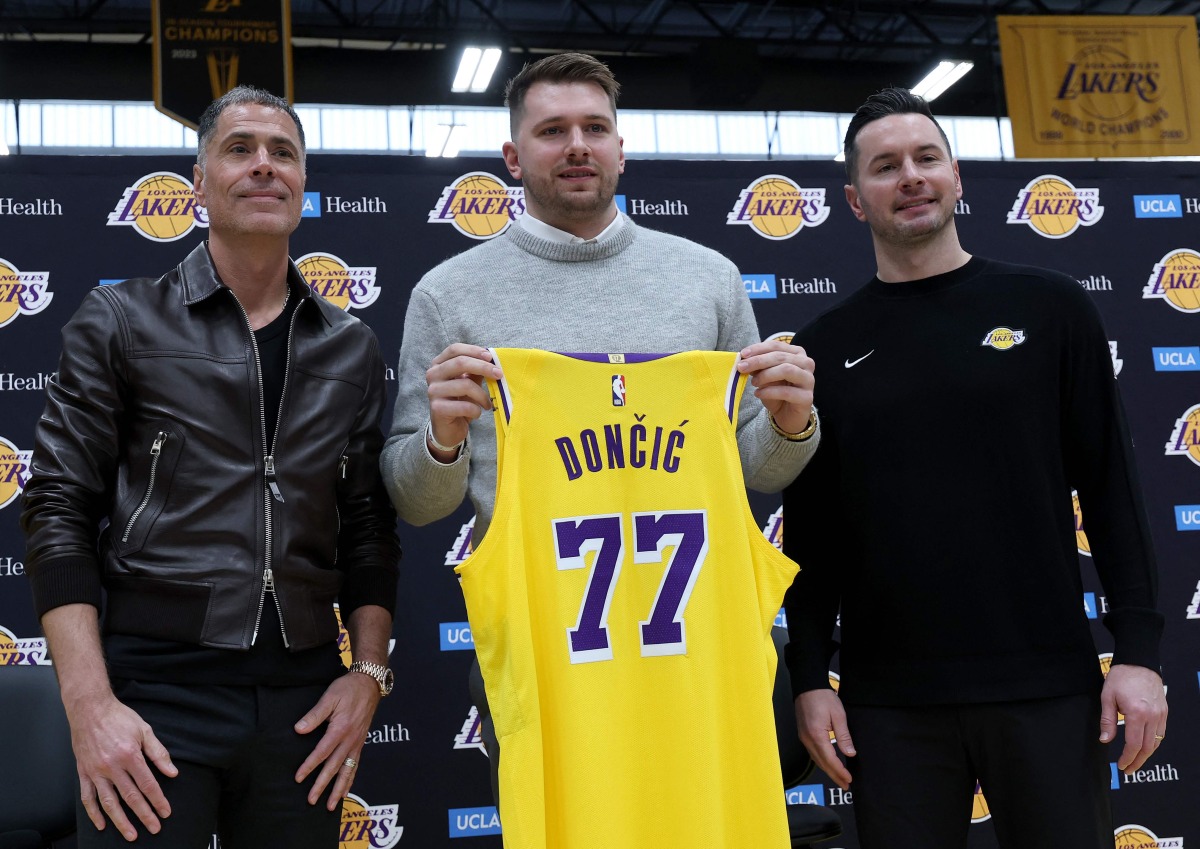 Luka Doncic (C) of the Los Angeles Lakers holds his new jersey while standing alongside general manager Rob Pelinka (L) and head coach JJ Redick (R) during a press conference at UCLA Health Training Center on February 04, 2025 in El Segundo, California. (Photo by Harry How / GETTY IMAGES NORTH AMERICA / Getty Images via AFP)
