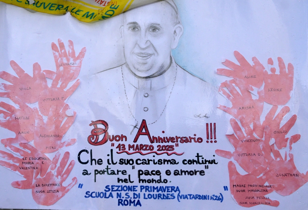 A picture shows a portrait of Pope Francis drew by school children at the statue of John Paul II outside the Gemelli hospital where Pope Francis is hospitalized with pneumonia, in Rome on March 13, 2025. (Photo by Tiziana Fabi / AFP)