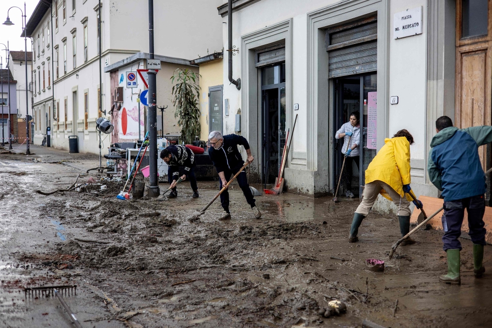 Residents and volunteers clean up mud and debris in a flooded street in Sesto Fiorentino, on March 15, 2025, one day after heavy rain hit the Florence region. (Photo by Federico Scoppa / AFP)