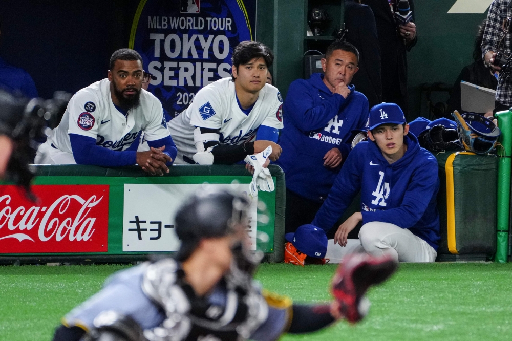 Los Angeles Dodgers' Shohei Ohtani (C), Teoscar Hernandez (L) and Roki Sasaki (R) watch from the dugout during the exhibition baseball game between the Los Angeles Dodgers and Hanshin Tigers at the Tokyo Dome in Tokyo on March 16, 2025. (Photo by Yuichi Yamazaki / AFP) 