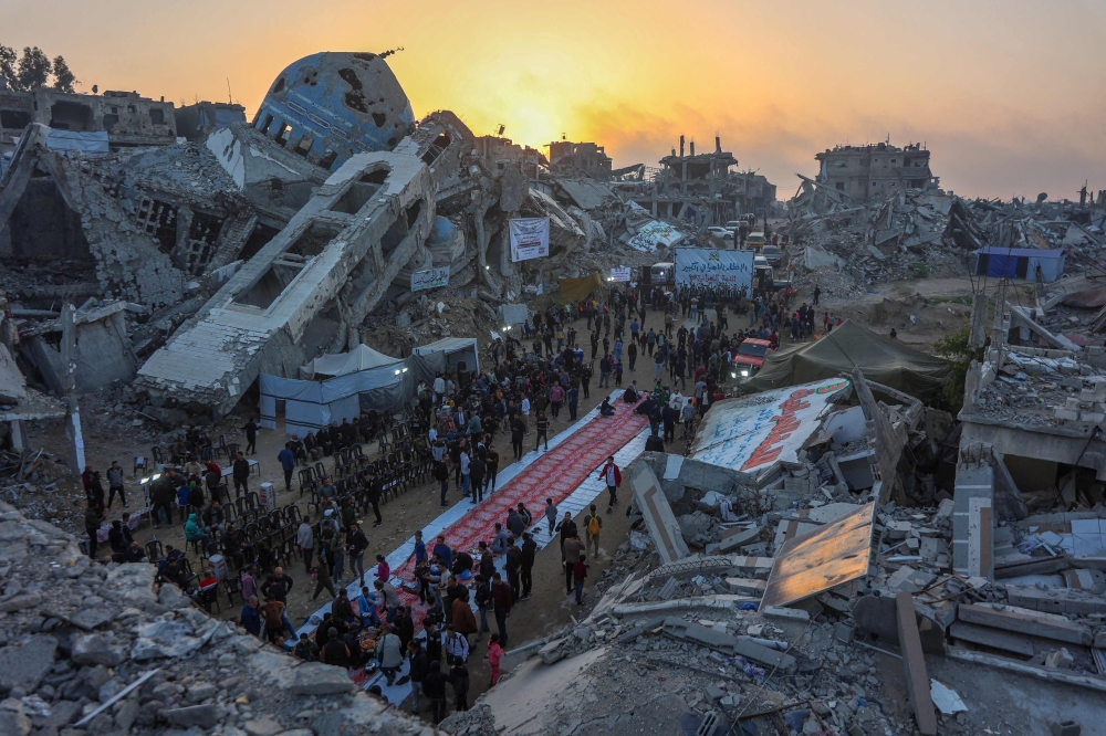 Palestinians gather for a mass fast-breaking iftar meal in front of the destroyed Salim Abu Muslim mosque in Beit Lahia in the northern Gaza Strip on March 15, 2025. (Photo by Omar Al-Qattaa / AFP)