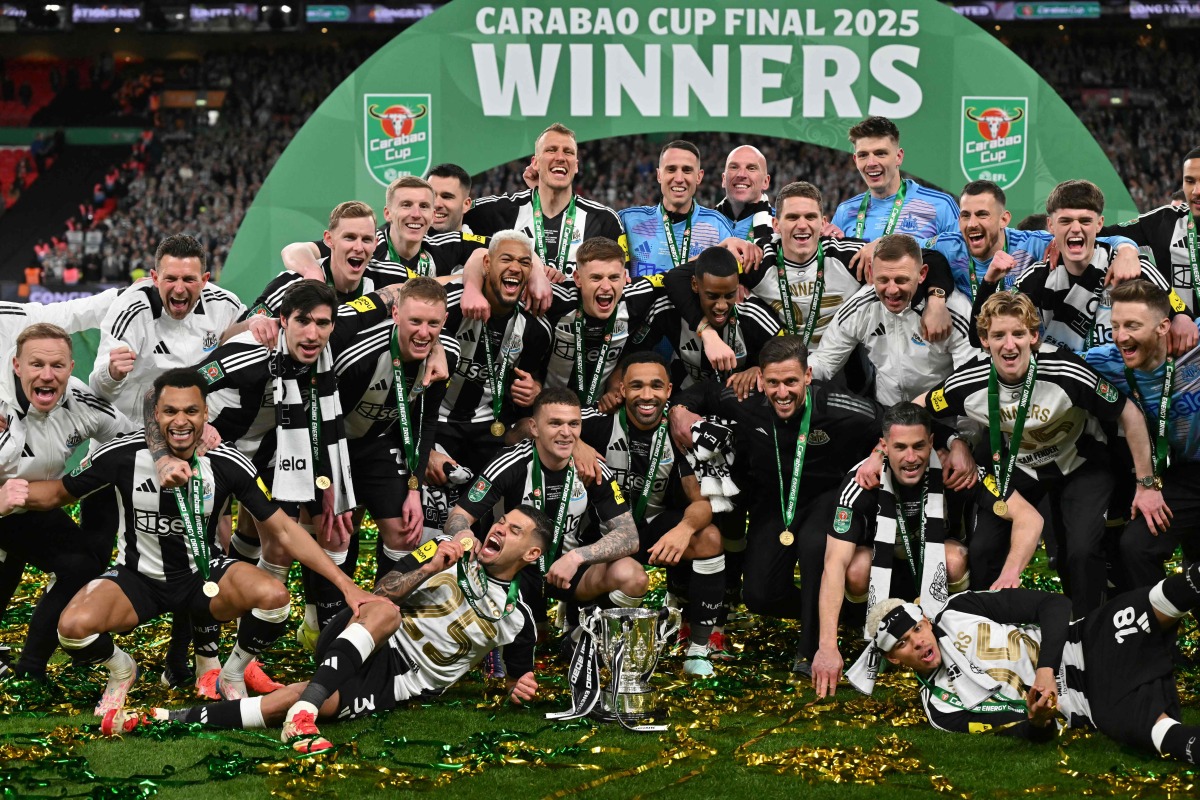 Newcastle United's players celebrate with the trophy on the pitch after the English League Cup final football match between Liverpool and Newcastle United at Wembley Stadium, north-west London on March 16, 2025. Newcastle won the game 2-1. (Photo by Glyn KIRK / AFP) 