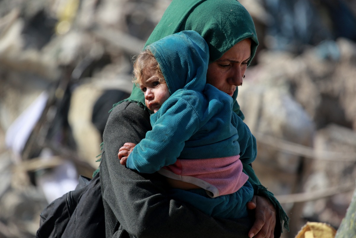 A Palestinian woman carries a baby as families leave the eastern sector of the Gaza Strip on the border with Israel following Israeli airstrikes that targeted northern and other parts of Gaza in the early hours of March 18, 2025. Gaza's civil defence agency said the death toll from a massive Israeli campaign launched throughout the Palestinian territory rose to more than 400 people, including children. Photo by Bashar TALEB / AFP.