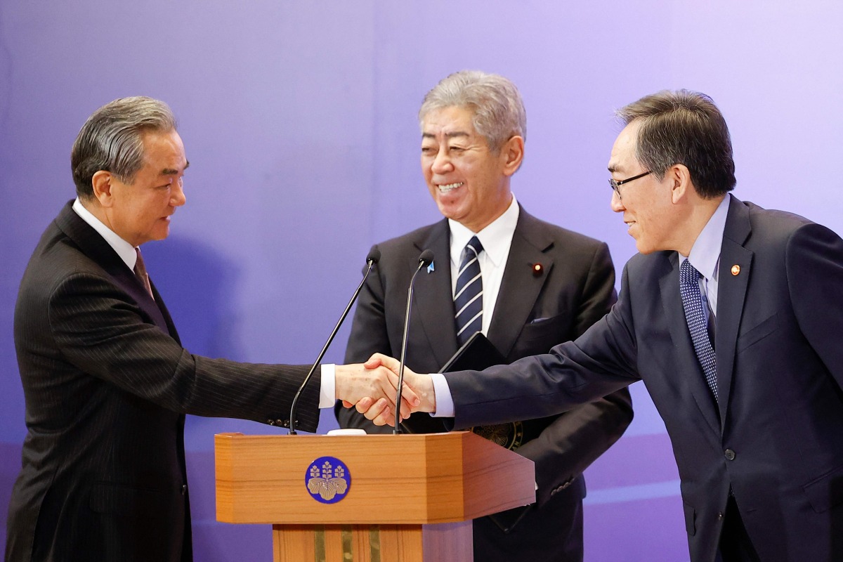 China's Foreign Minister Wang Yi (L) and South Korea's Foreign Minister Cho Tae-yul (R) shake hands as Japan's Foreign Minister Takeshi Iwaya looks on during a joint press conference after their meeting during the 11th Trilateral Foreign Minister's Meeting (Japan-China-ROK) in Tokyo on March 22, 2025. (Photo by Rodrigo Reyes Marin / POOL / AFP)
