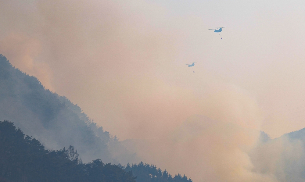 Helicopters try to extinguish a fire after a wildfire broke out in the southeastern county of Sancheong on March 22, 2025. (Photo by YONHAP / AFP)