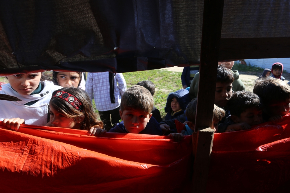 Palestinian children look into a tent as workers search through the rubble of a building at the site of an Israeli strike in Khan Yunis in the southern Gaza Strip on March 23, 2025. (Photo by AFP)
