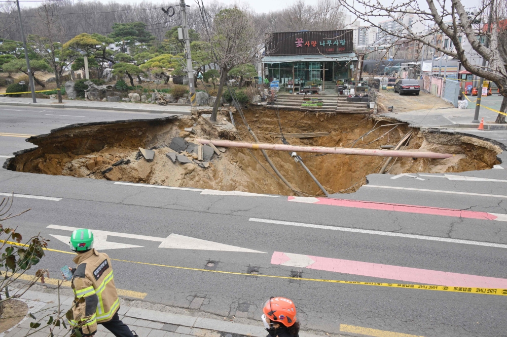 Rescue workers walk past a sinkhole outside a plant shop on a road in Seoul on March 25, 2025. (Photo by Anthony Wallace / AFP)