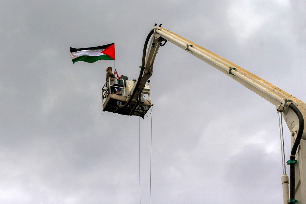 A demonstrator being raised by a crane holds up a Palestinian flag during a rally in solidarity with Palestinians in the Gaza Strip and in condemnation of US strikes, in Yemen's capital Sanaa on April 11, 2025. (Photo by Mohammed Huwais / AFP)
